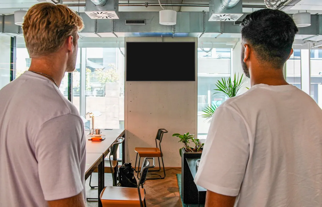 A screen on the wall of a coworking space, with two people looking at it