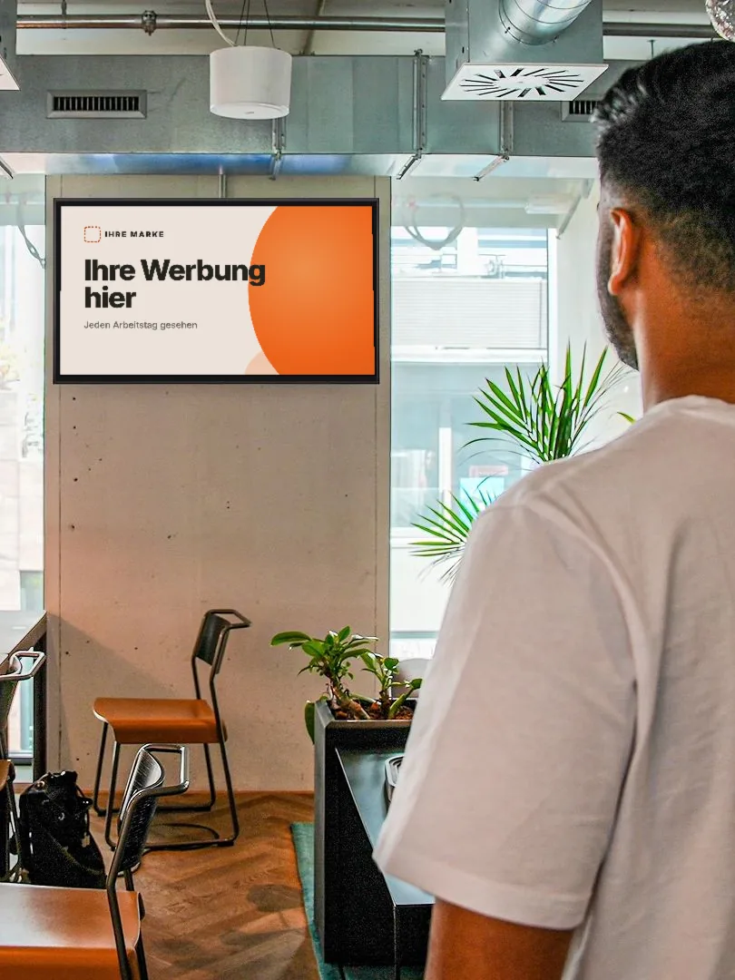 Beispielfoto: ein Bildschirm an der Wand eines Coworking Space mit der Musteranzeige „Ihre Werbung hier“, ein Mann schaut in seine Richtung