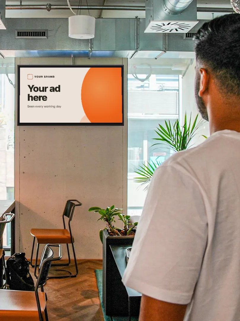 Representative photo: a screen on the wall of a coworking space showing a mock-up ad that reads Your ad here, with a man looking towards it