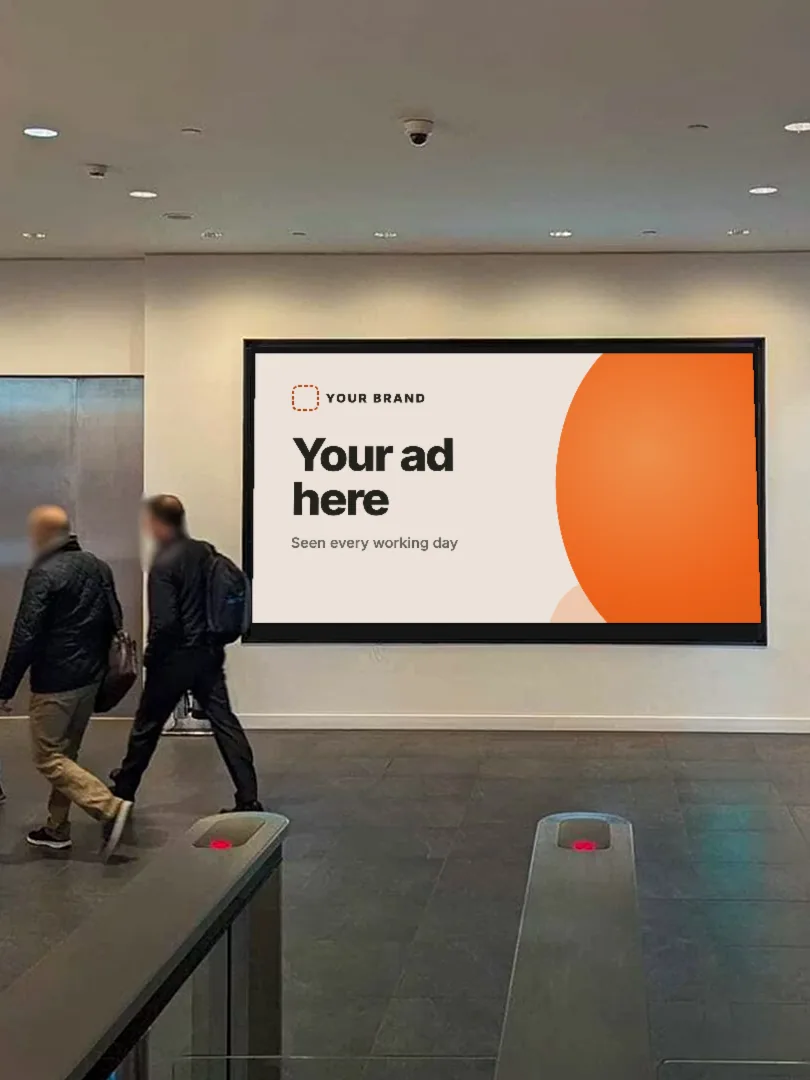 Representative photo: two people walking past a large screen in an office lobby that shows a mock-up ad
